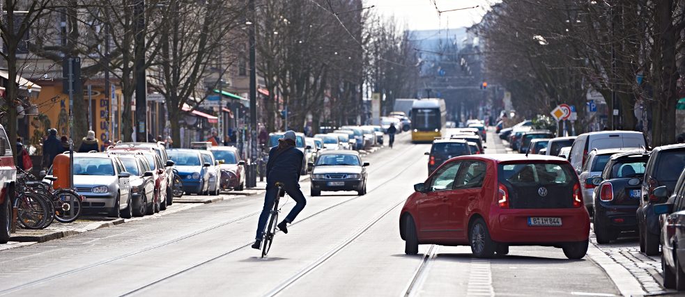 Un ciclista nel traffico evita una macchina che sta manovrando per parcheggiare.