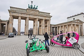 Ein Gruppenfahrrad und ein Velotaxi stehen vor dem Brandenburger Tor in Berlin