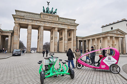 Ein Gruppenfahrrad und ein Velotaxi stehen vor dem Brandenburger Tor in Berlin.