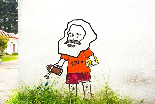 Karl Marx in Shorts und T-Shirts gießt sinnbildlich das wachsende Gras