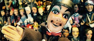 Guignol - Eine lächelnde Marionette vor anderen Puppen im Hintergrund