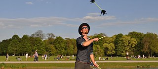 A young man juggling flowersticks in a park.