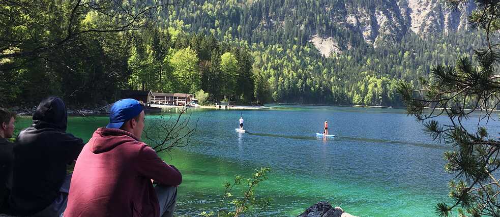 Junge Männer blicken auf einen See in der Sonne.