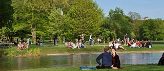 許多人們在大太陽底下坐在慕尼黑英國公園的施瓦賓河畔