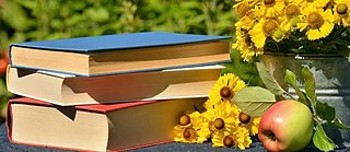 A small stack of books, an apple and yellow flowers.