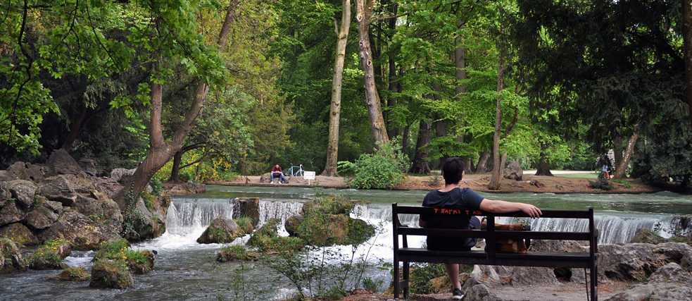 Ein Mann sitzt auf einer Bank und blickt auf einen Wasserfall.