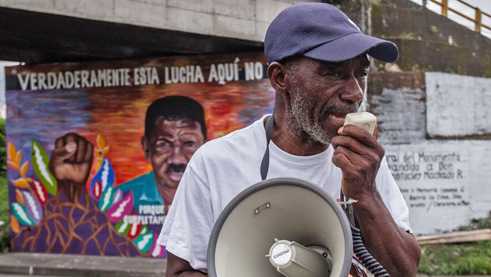 A companion of Temístocles Machado in front of a mural to his memory