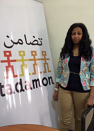 Fateema Idris, Executive Director of the Egyptian Multicultural Refugee Council (Tadamon), standing next to a large sign that has "Tadamon" written on it.