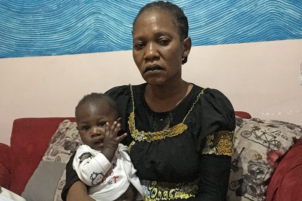 Rose Kuku, une femme assise sur un canapé rouge avec son jeune fils Yusuf sur ses genoux.