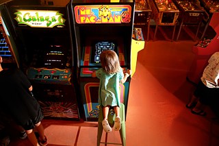 Die wohl erste Games-Heldin überhaupt war Ms Pac-Man: Ein Mädchen sitzt vor einem Ms Pac-Man-Spieleautomaten.