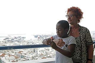 Eine ältere Frau, Hassina, mit ihrem Sohn Fayçal im Arm, auf dem Balkon mit Blick auf die Bucht von Algiers