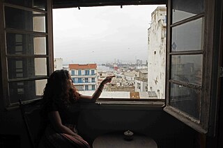 Lamia, a young woman, at the window of an Algerian apartment overlooking the Port of Algiers