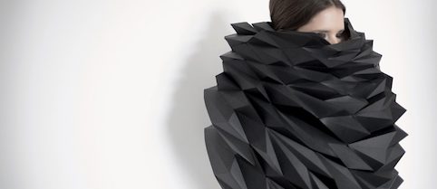 A woman wears an artistically folded top with an extremely high collar that covers half her face.