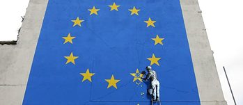 Street art by Banksy: a man on a ladder chiselling away at one of the stars on the European flag. 
