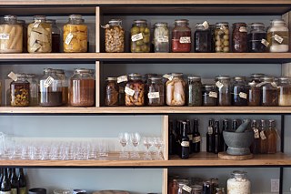 A wall of preserves and pickles line the wall in the restaurant 