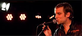 Jens Friebe mit Mikrofon und Bühnenbeleuchtung