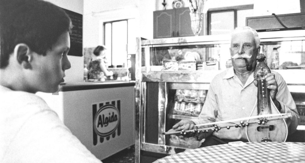 Ένας ηλικιωμένος άντρας παίζει την κρητική λύρα του. Ο εγγονός του τον παρακολουθεί ενθουσιασμένος σε ένα καφενείο στην Κάρπαθο. Πολλά καφενεία της ελληνικής υπαίθρου διατηρούν έτσι την τοπική παράδοση.