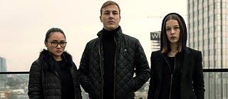 "Bad Banks - The Lion's Den": Jana (Paula Beer), Adam (Albrecht Schuch) and Thao (Mai Duong Kieu), dressed in black, stand side by side on the roof terrace of a skyscraper overlooking Frankfurt and pose for the camera.