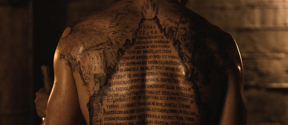 A big tattoo with a Latin inscription on the back of a man 
