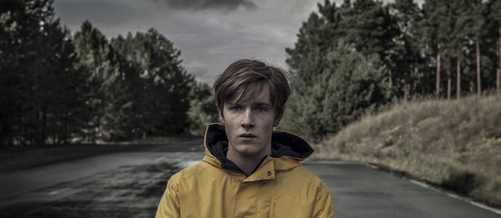 Jonas Kahnwald (played by Louis Hofmann) is standing alone in the middle of a wide street.