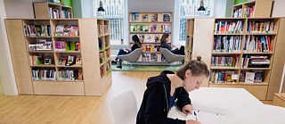 Three people in the library: two reading in armchairs while one makes notes at the table.