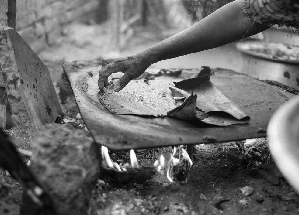 Photo en noir et blanc d'une main manipulant un morceau de tissu posé sur un morceau de métal au-dessus d'un feu.