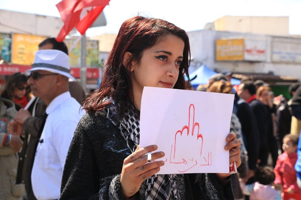 A young woman at a protest against the conservative Islamic Ennahda party holding up a sign.
