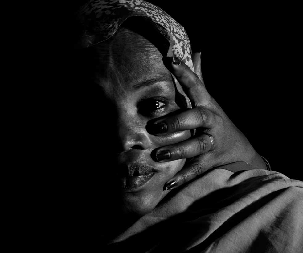 Black and white close-up photo of a woman's face, half her face is in the shadow, a hand from the back is on her cheek.