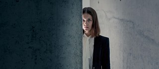 Bad Banks: Jana Liekam (Paula Beer) steht halb versteckt hinter einer Betonwand inmitten eines sonst leeren, tristen Raumes.