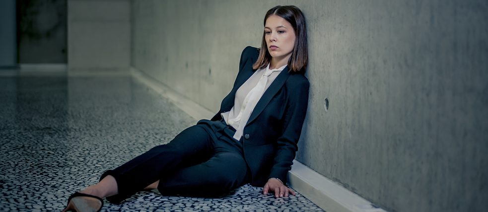 „Bad Banks“: Jana Liekam (Paula Beer) sitzt erschöpft auf dem Boden in einem großen, leeren Raum. Sie lehnt sich gegen die karge Betonwand.