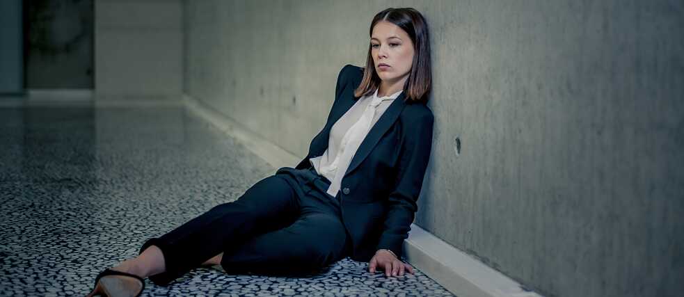 „Bad Banks“: Jana Liekam (Paula Beer) sitzt erschöpft auf dem Boden in einem großen, leeren Raum. Sie lehnt sich gegen die karge Betonwand.
