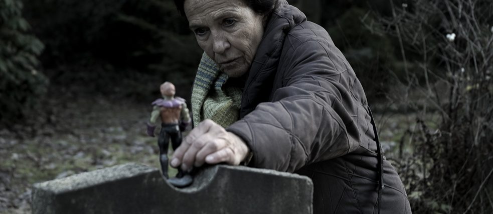 DARK Una señora mayor pone una figura de juguete en una lápida...