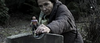Dark production still: An old women places an action figure on a gravestone.
