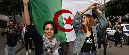Une manifestation avec, au centre de l'image, deux jeunes femmes agitant le drapeau algérien entre elles.