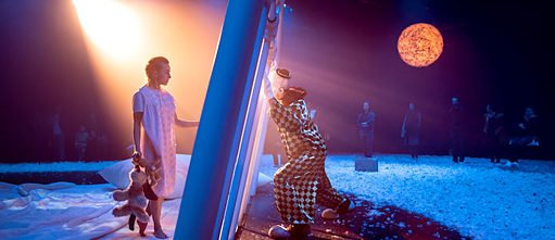 Sur une scène aux couleurs de la nuit, une fille tenant à la main un animal en peluche se tient debout en face d'un clown, ils sont séparés par une barrière en métal