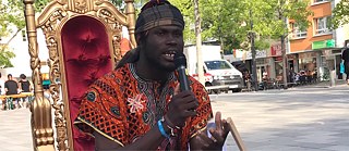 Junger Mann in afrikanischer Tracht auf Thronsessel mit Mikrofon