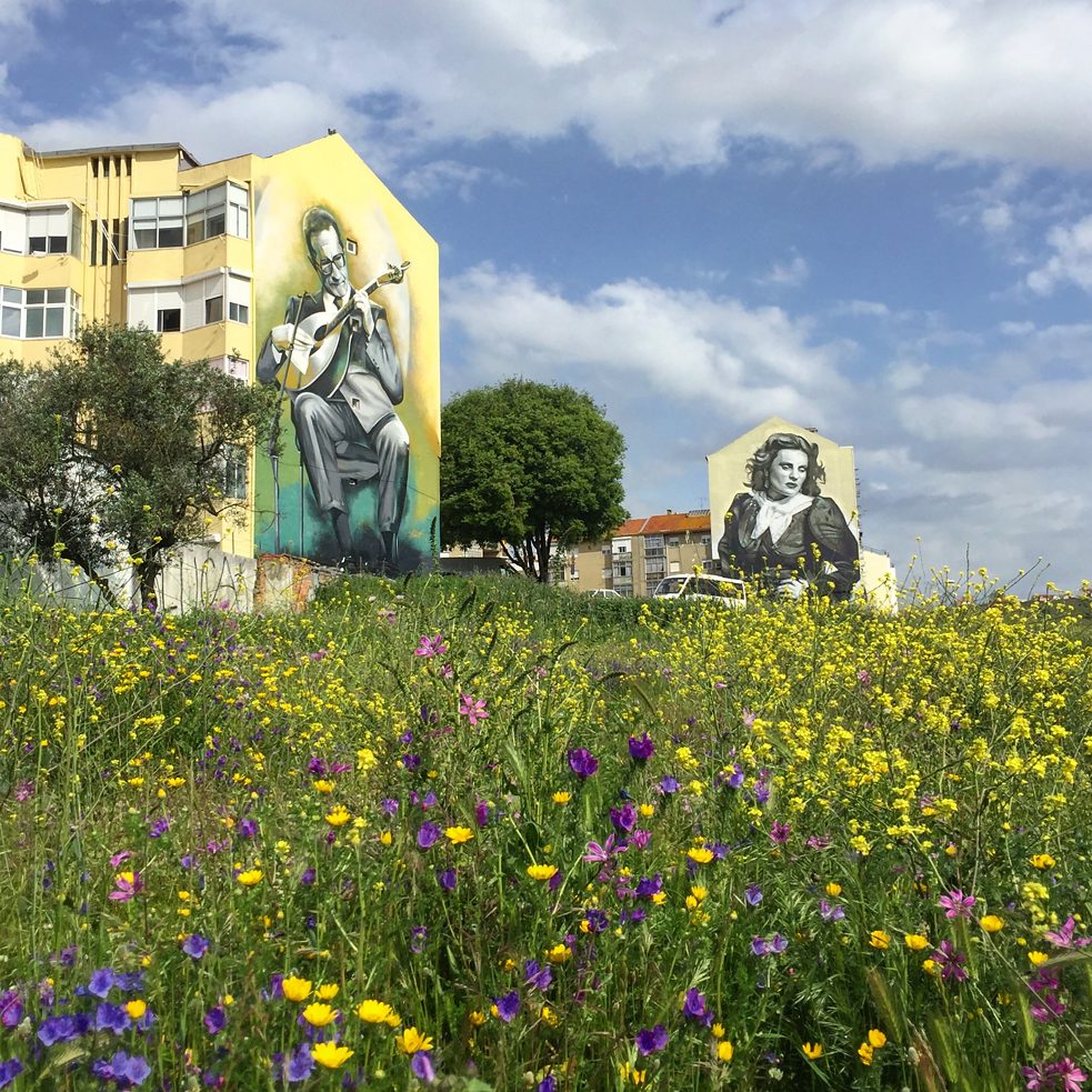 <b>Musikalische Legenden (Amadora, Portugal)</b><br><br>Von underground zur anerkannten Kunst: In der letzten Dekade entwickelten sich die großen Wandgemälde auf den Fassaden von Wohn- und Geschäftshäusern zu einer urbanen Marke im Großraum Lissabon. Früher verboten, sind die großflächigen Werke von Künstlern aus aller Welt heute aus dem Stadtbild nicht mehr wegzudenken und sorgen in Lissabon und seinen Vorstädten für ein bunteres Stadtbild. Oft greifen sie Themen und Persönlichkeiten der portugiesischen Geschichte und Kultur auf, wie die beiden Wandgemälde des Künstlers Odeith, die zwei der berühmtesten Ikonen der portugiesischen Musik zeigen: Carlos Paredes und Amália.