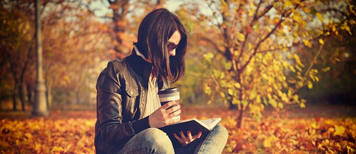 Woman with coffee cup reading a book, sitting on leaves. Vintage photo, Stock image