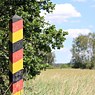 Ein Grenzpfahl an der ehemaligen innerdeutschen Grenze in schwarz, rot, gold auf einer Wiese.