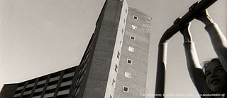 Photographie en noir et blanc d’un bâtiment avec au premier plan une jeune fille qui joue