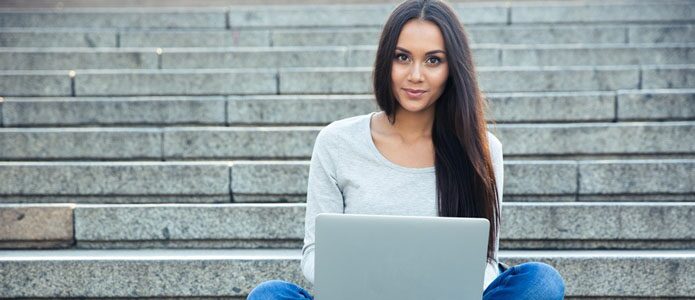 Eine junge Frau sitzt auf einer Treppe und hält ihr Laptop