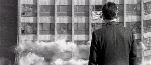 Schwarz-weiß Aufnahme eines Mannes, den Einsturz eines Gebäudes beobachtet.