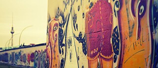 Abstraktes Graffiti auf Berliner Mauer mit Fernsehturm im Hintergrund.