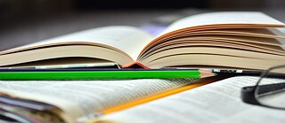 Man sieht ein aufgeschlagenes Buch und Stift