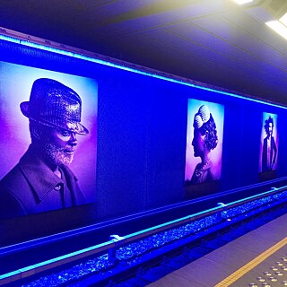  <b>Stephan Vanfleteren – Mode dans le métro, 2009 (Bruxelles, Belgique)</b><br><br>Nous sommes dans la station de métro Gare de l’Ouest à Molenbeek-Saint-Jean, Bruxelles. A l’extérieure la station ne semble pas très spéciale, mais à l’intérieure on trouve des trucs extraordinaires. Des photos de Stephan Vanfleteren se trouvent sur les murs du quai en direction de Beekkant. On peut voir 13 personnes ordinaires décorés par des grandes belges maisons de mode, qui montrent le cosmopolitisme de Bruxelles. 