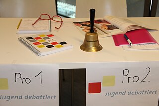 Jugend debattiert - Tisch mit Glocke, pro und contra Seite bei Debatte