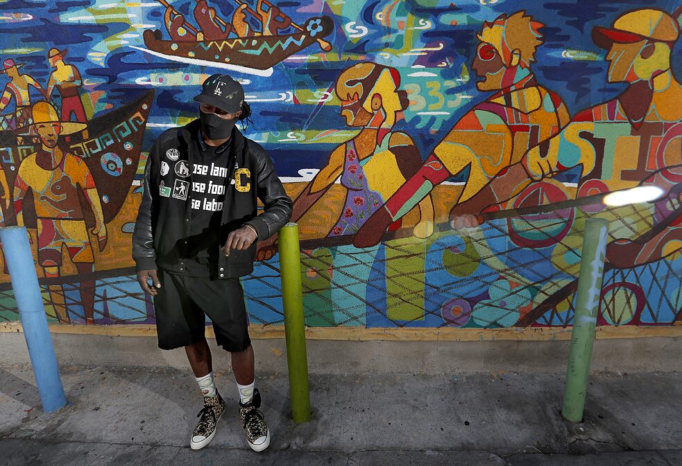 The artist ShowzArt stands in front of the mural “The Living Water,” to which he contributed, near the corner of Fifth Street and Central Avenue in Los Angeles