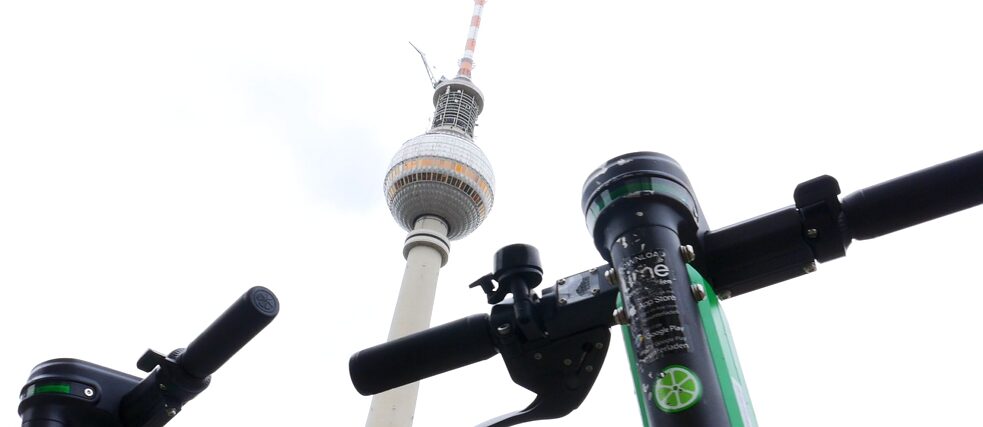 Die Lenker von zwei E-Tretrollern vor dem Fernsehturm in Berlin