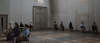 Scène de la pièce de théâtre : les acteurs et actrices sont assis dans une pièce vide sur des chaises face à des murs vides sur lesquels l’on voit des traces d’œuvres qui y étaient auparavant accrochées.