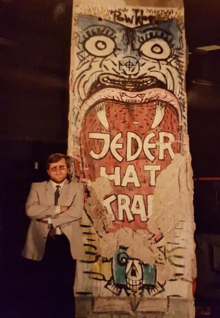 Peter Kubiak steht neben seinen Stück Berliner Mauer in Sydney (circa 1990)
